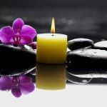 Eine Kerze mit schwarzen Steinen im Wasser mit Lotusblüte